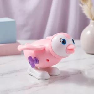 Cute pink penguin wind-up toy with white belly and side winding key standing on a smooth surface.