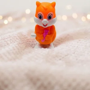 Cute orange squirrel wind-up toy holding a pink carrot standing on a light-colored surface.