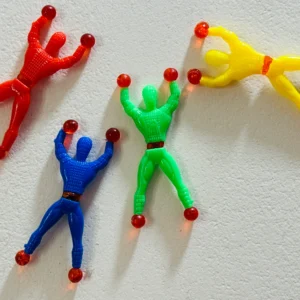 Four colorful Sticky Wall Crawler Spider-Man toys in red, blue, green, and yellow tumbling down a white textured surface.